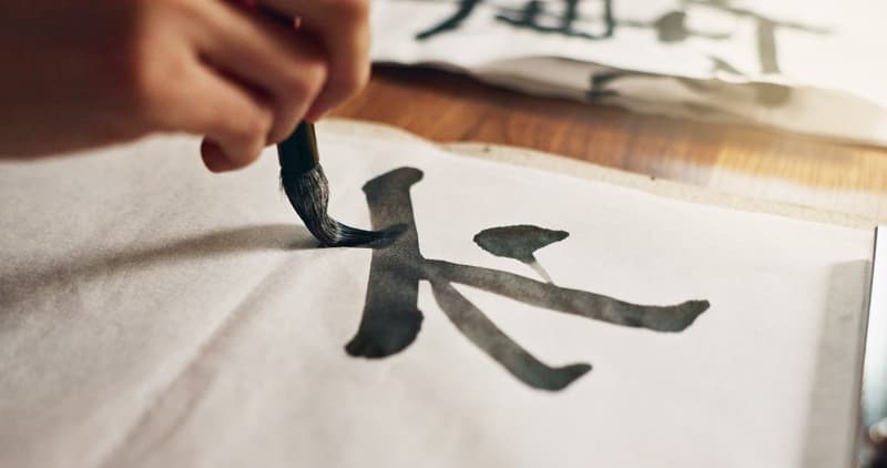 A brush writes Japanese calligraphy on paper.